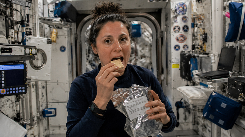 フリーズドライ製法の宇宙食を食べている女性宇宙飛行士のイメージ画像